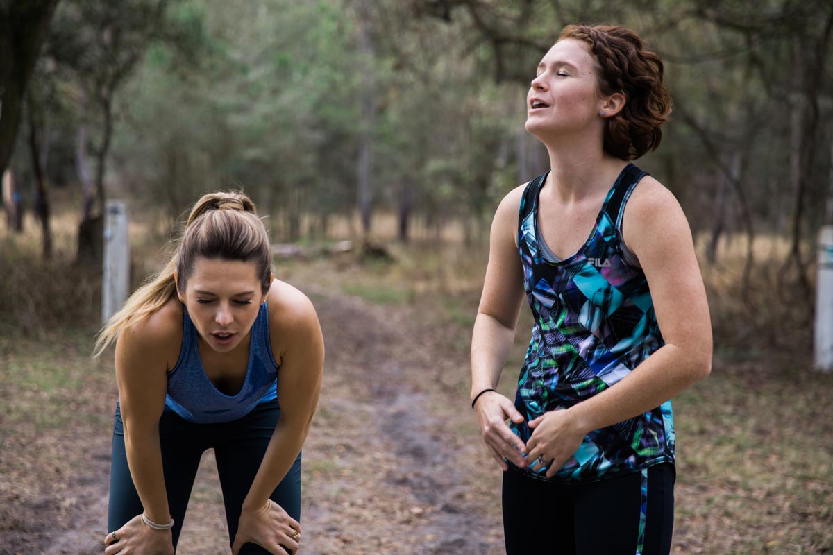 Women in forest running on a trail in workout clothes.