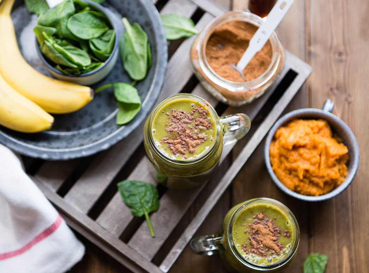 2 glass mugs with pumpkin smoothie topped with pumpkin pie spice next to a mug of pumpkin puree and a jar of spice.