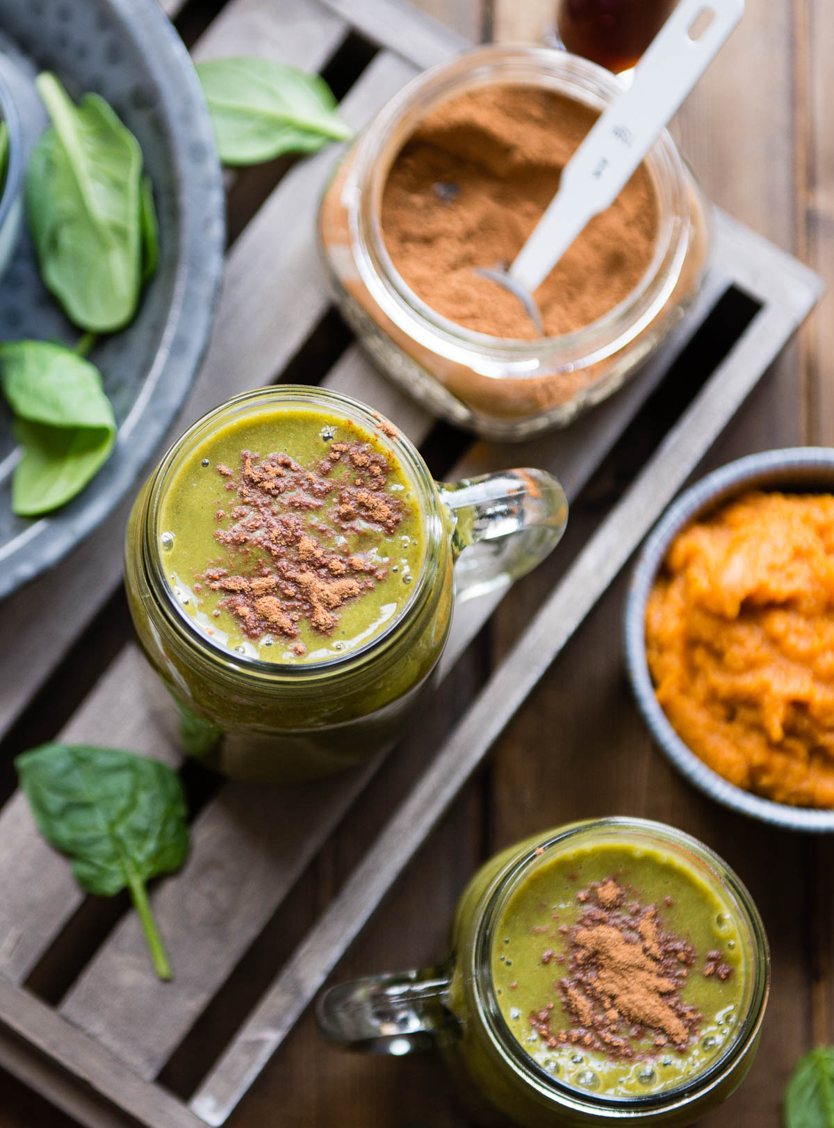 2 glass jars of green smoothie topped with pumpkin pie spice.