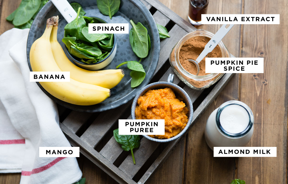 labeled ingredients for a pumpkin smoothie recipe including spinach, vanilla extract, pumpkin pie spice, pumpkin puree, almond milk, banana and mango.