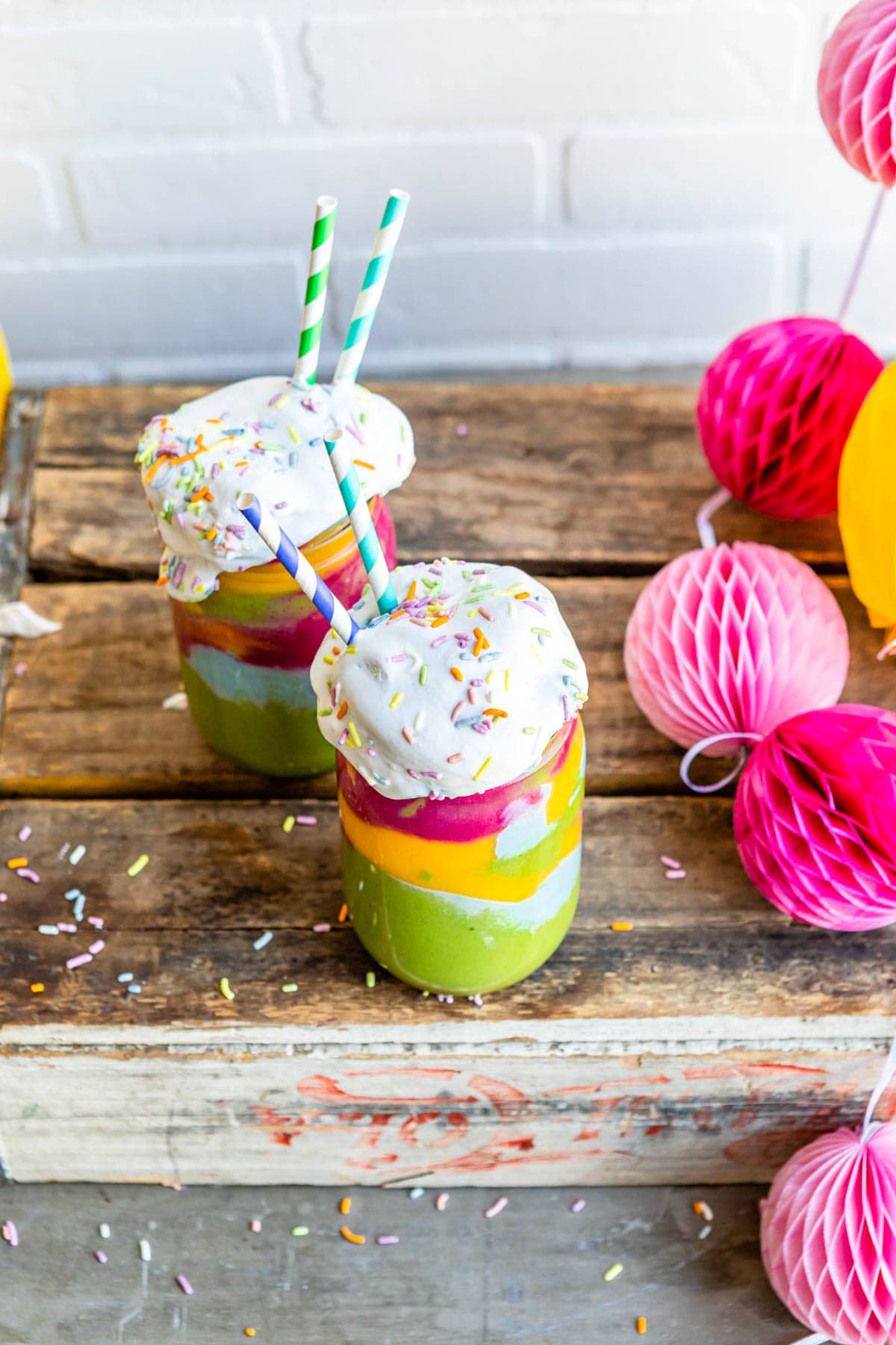 fun party dessert in a glass jars with sprinkles and coconut whipped cream on top as well as paper straws.