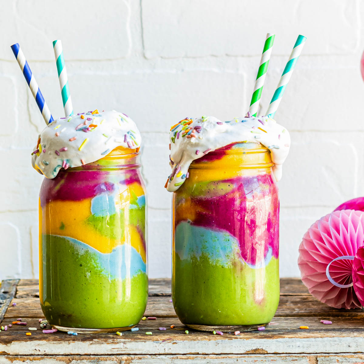 rainbow smoothies in glass jars with coconut whipped cream and paper straws