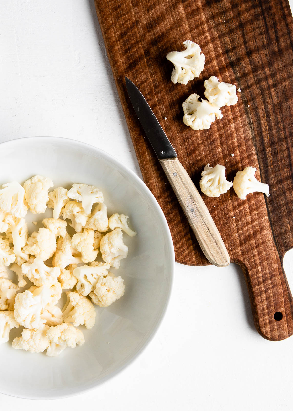 chopping cauliflower on a wooden cutting board then placing in a white bowl.