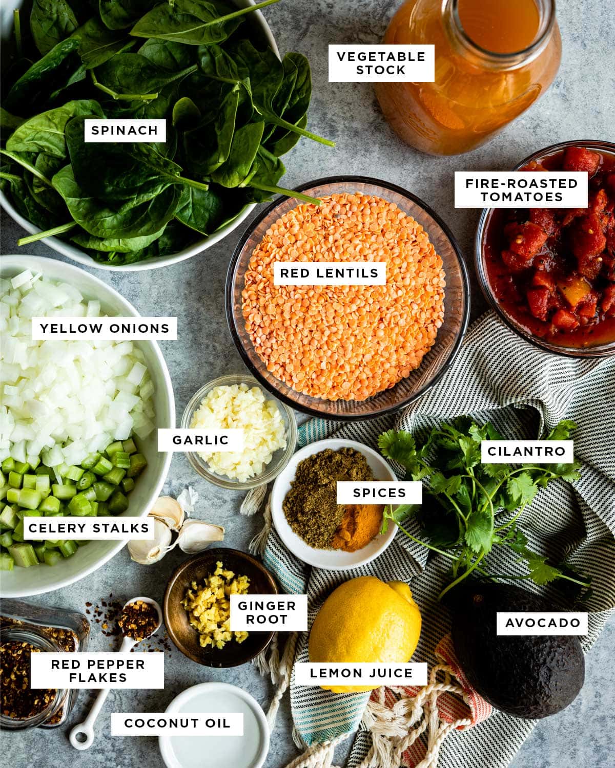 labeled ingredients for a hearty soup including vegetable stock, fire-roasted tomatoes, red lentils, cilantro, spices, lemon juice, avocado, ginger root, coconut oil, red pepper flakes, celery, garlic, yellow onions and spinach.