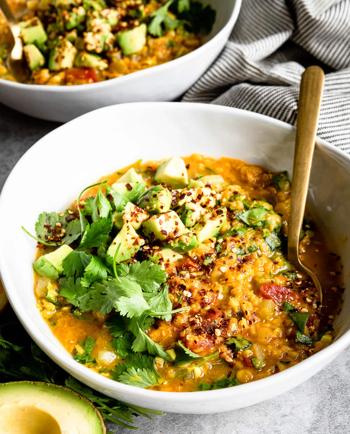 white bowl of red lentil soup with cilantro, avocado and red pepper flakes on top.