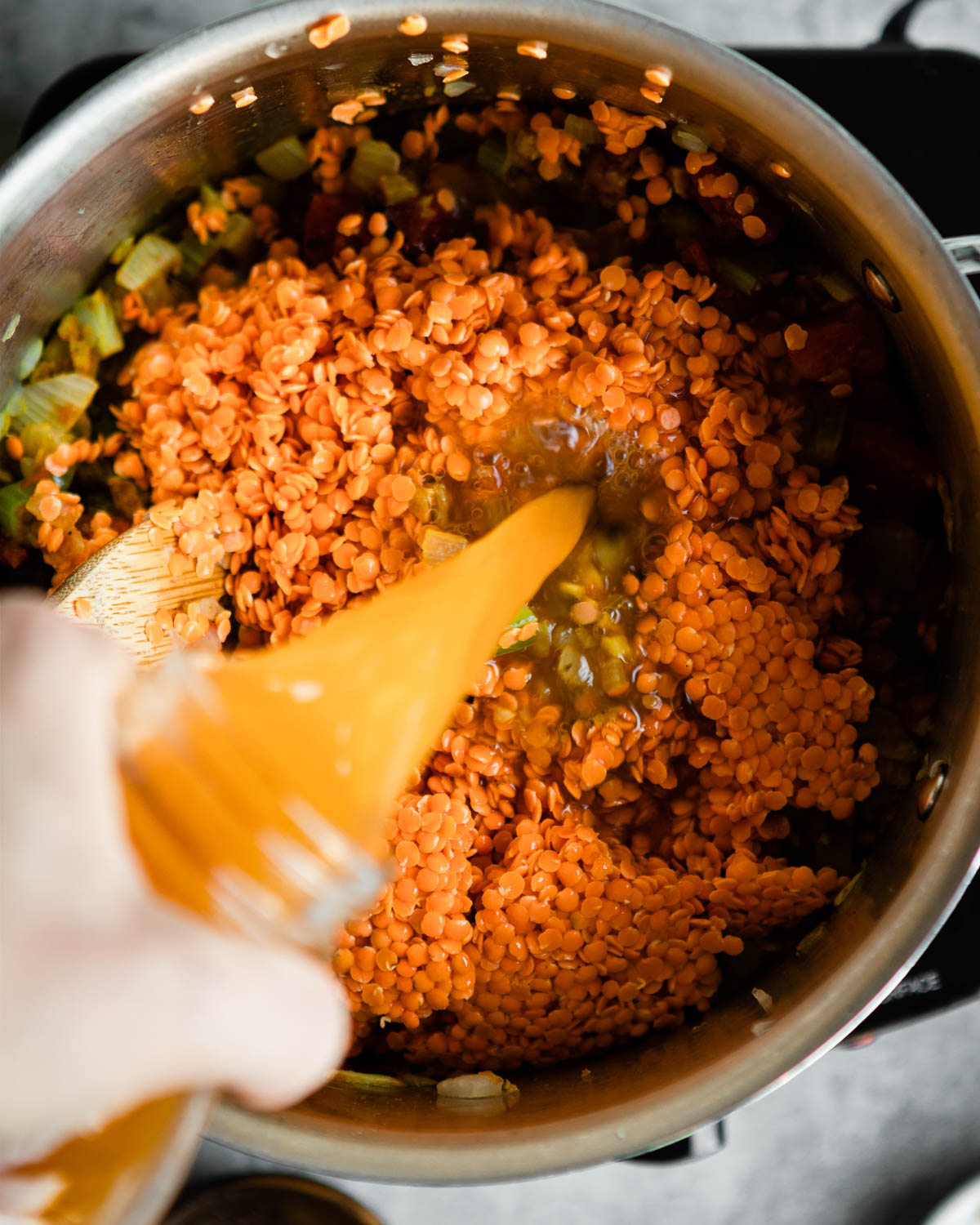 pouring vegetable stock into a pot with red lentils