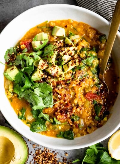 red lentil soup in a white bowl, topped with fresh avocado and a gold spoon.