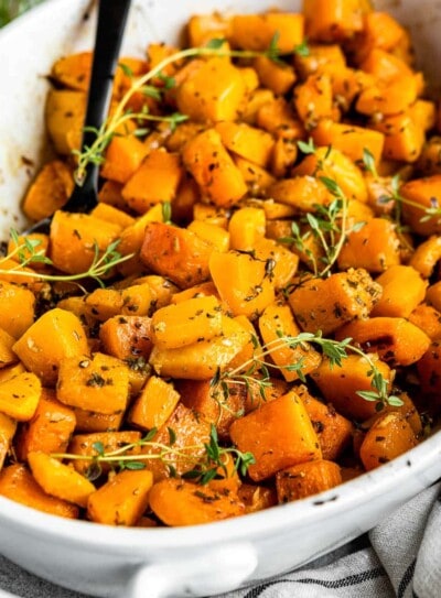 ceramic dish of roasted butternut squash topped with fresh herbs.