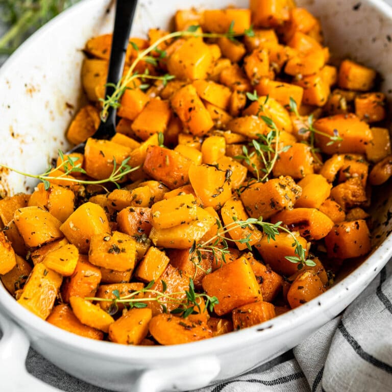 ceramic dish of roasted butternut squash topped with fresh herbs.