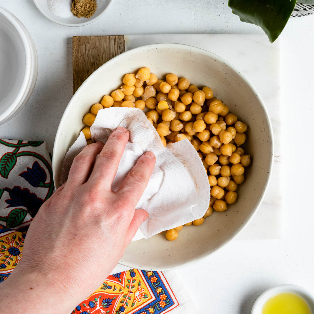 white hand using a paper towel to dry a bowl of chickpeas.