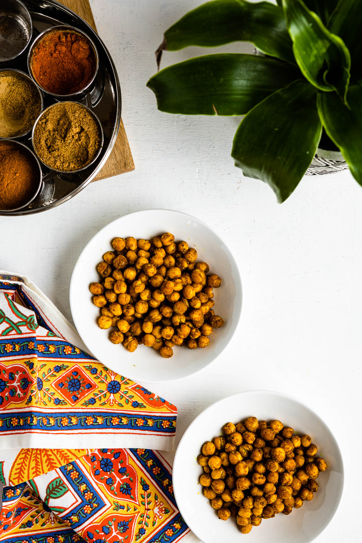 2 white bowls of roasted chickpeas next to a colorful tea towel.