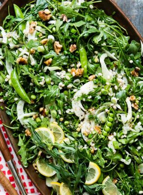 Fresh green arugula salad with lemon slices and walnuts on a wooden platter.