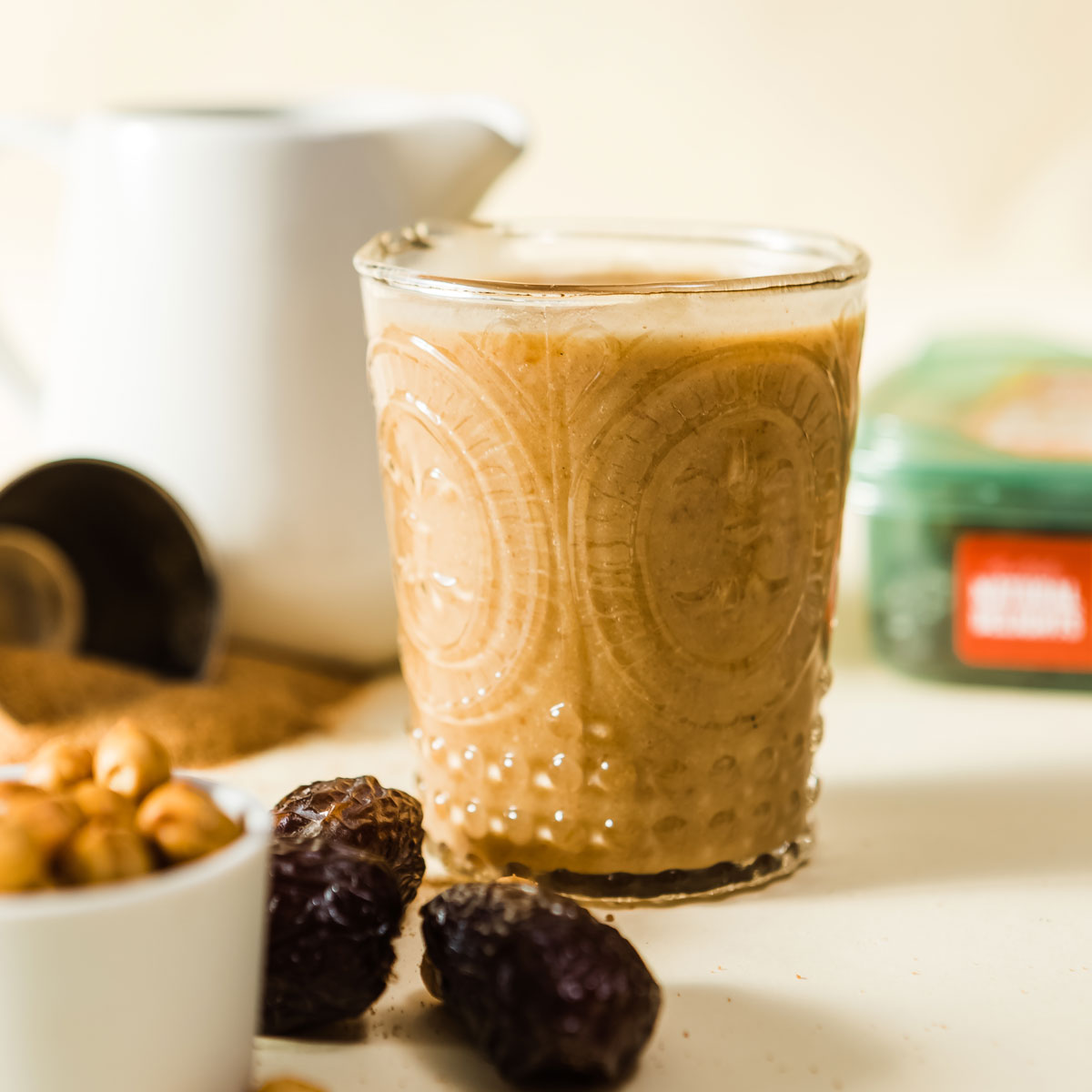 Salted caramel protein shake in a festive etched glass next to a bowl of cashews and some pitted medjool dates.