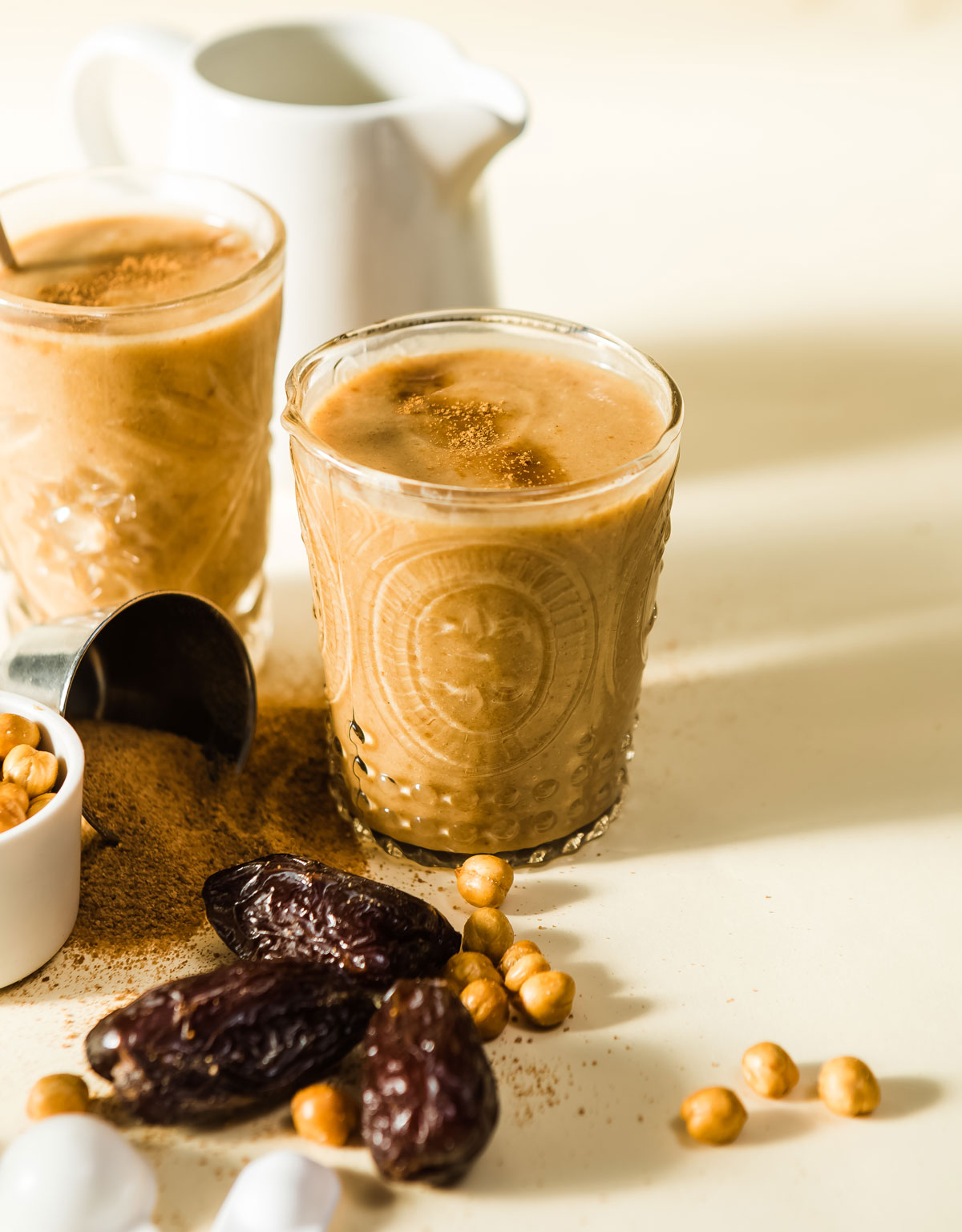 Festive glasses of salted caramel protein shake on counter with dates and garbanzo beans.