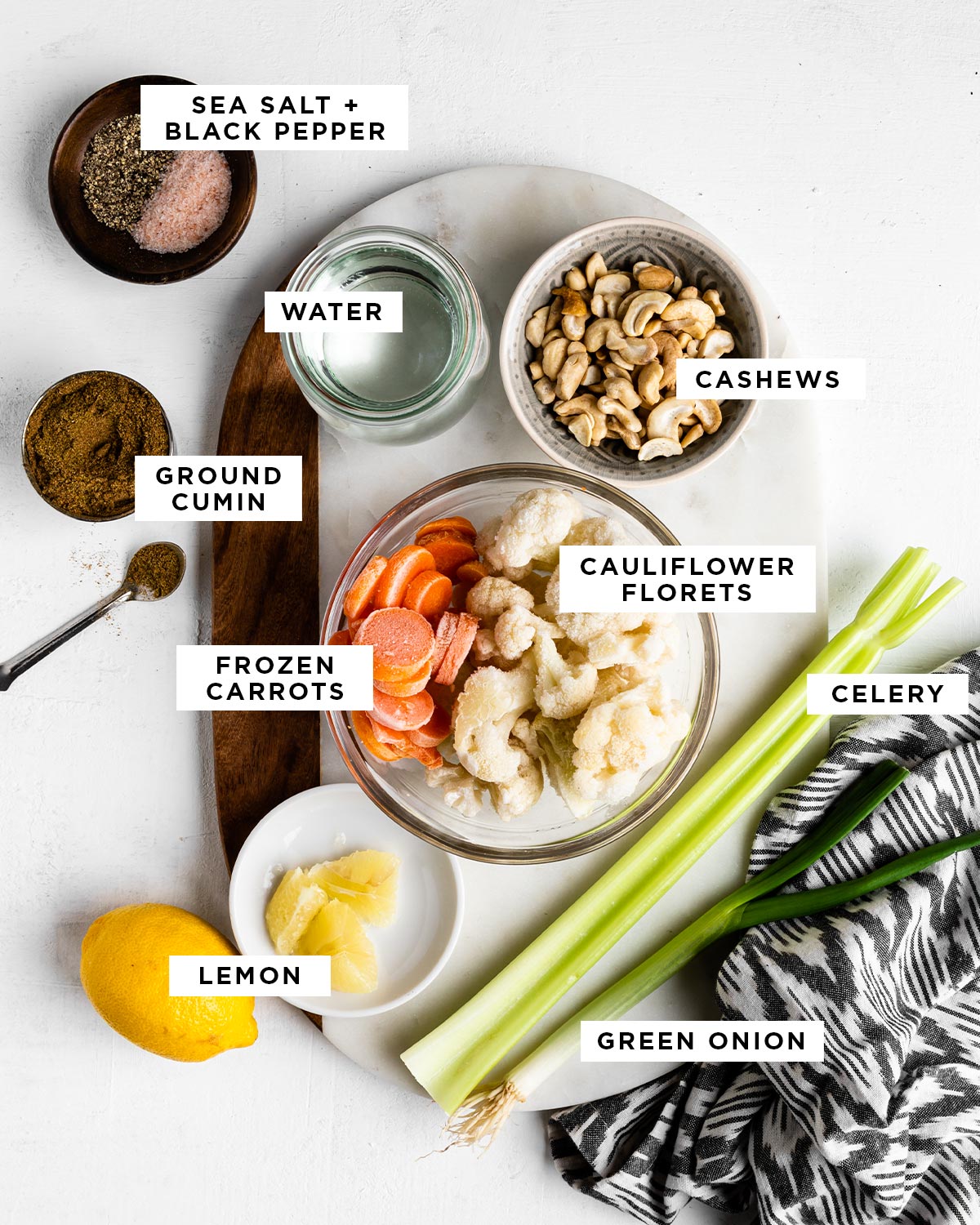 labeled ingredients for a savory beverage including sea salt, black pepper, water, cashews, ground cumin, cauliflower florets, frozen carrots, celery, lemon and green onion.