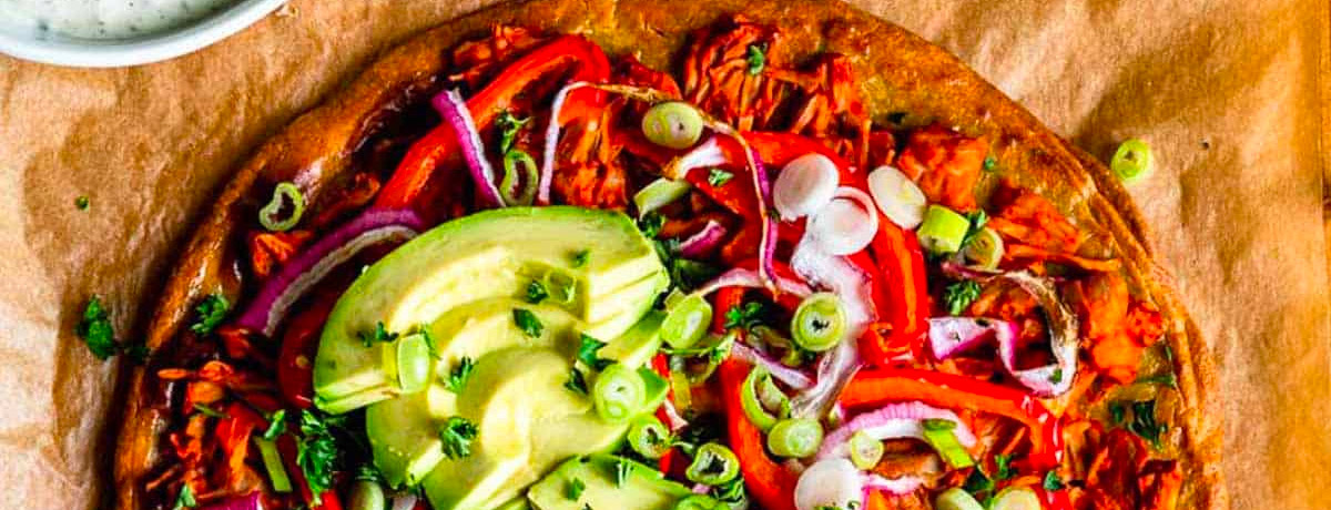 overhead shot of shredded jackfruit pizza with peppers, avocado, green onions, purple onions, and more