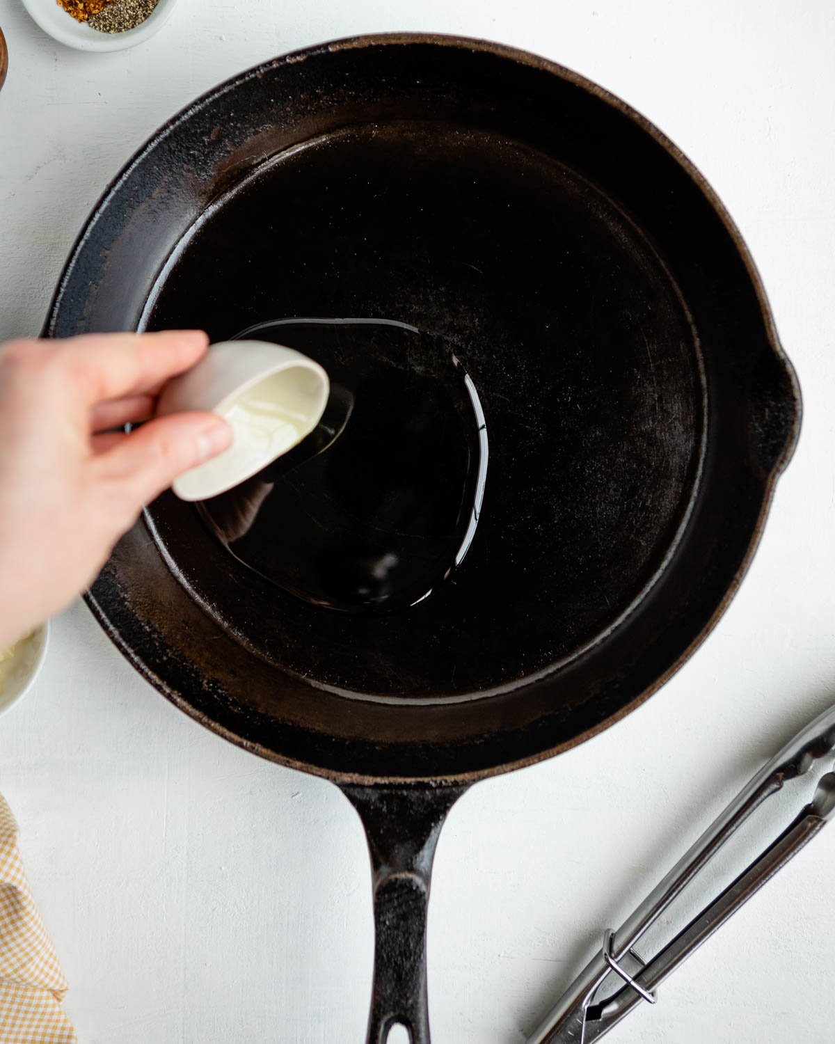A hand pouring oil into a cast iron skillet.