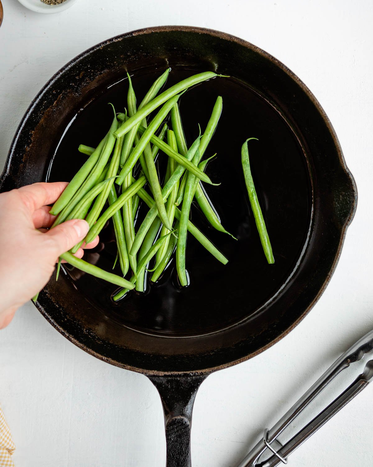 A hand adding raw green beans to a cast iron skillet.
