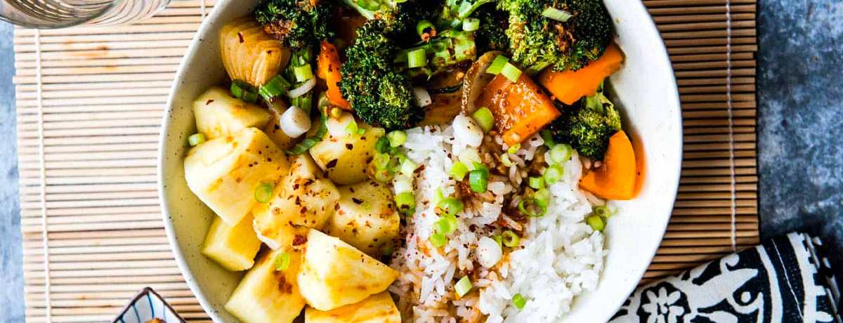 teriyaki bowl with cooked rice, pineapple, broccoli, carrots sitting on a bamboo mat