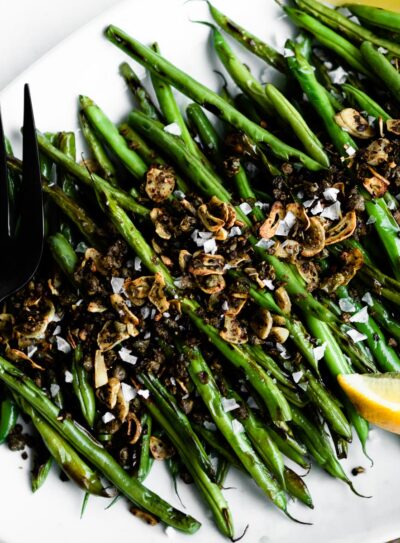 blackened green beans on a white serving tray topped with capers and garlic.