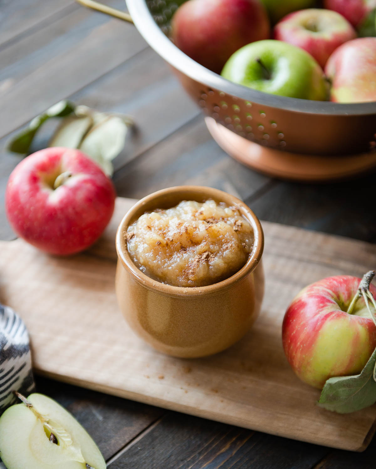 brown ceramic bowl full of crockpot applesauce topped with cinnamon sitting on a wooden cutting board.