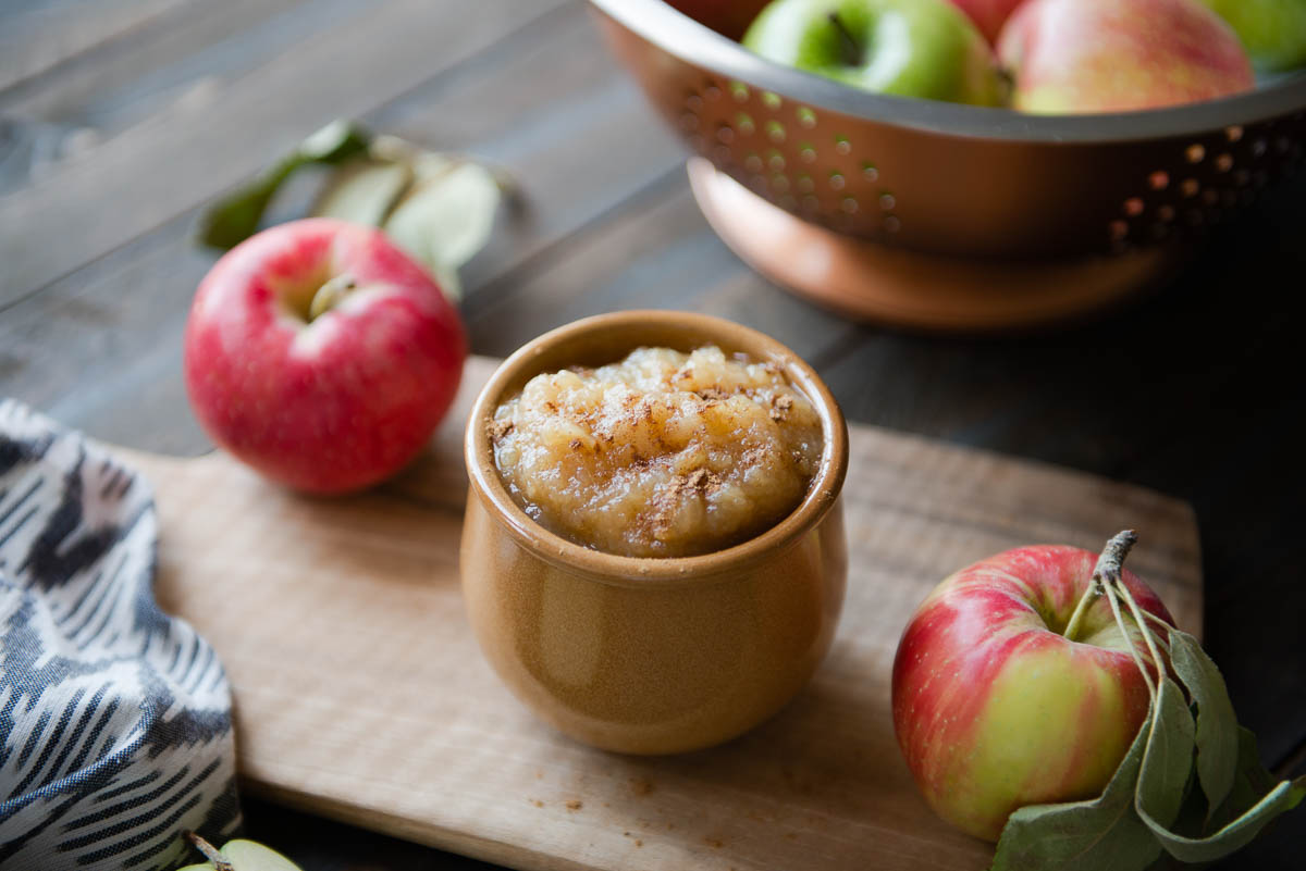 brown ceramic bowl full of slow cooker applesauce topped with cinnamon sitting on a wooden cutting board.