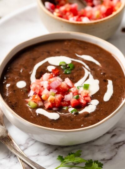 A bowl filled with spicy black bean soup, swirls of vegan sour cream, and salsa.