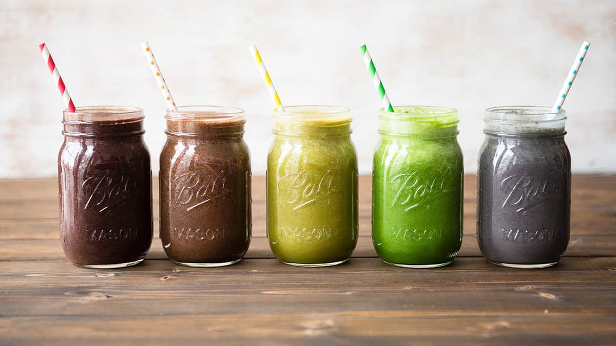 Colorful smoothies in mason jars with striped straws on wooden surface.