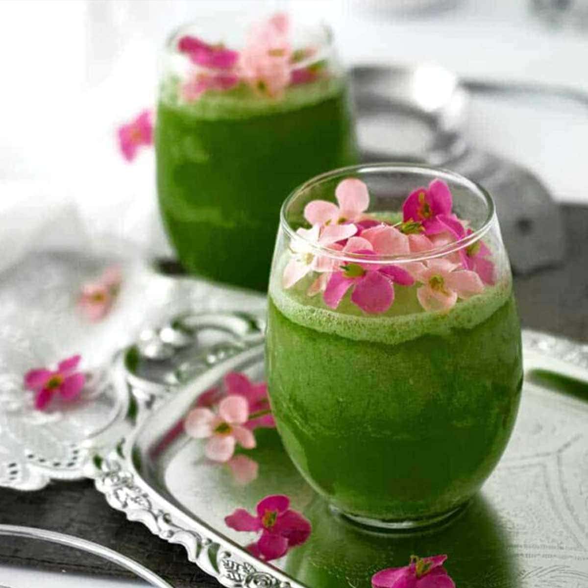 green smoothie for pregnancy in a round glass topped with pink flowers and sitting on a silver tray.