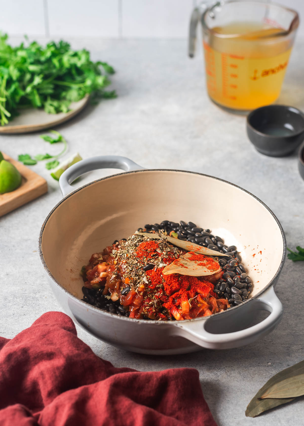 Dried black beans, herbs and spices in a gray pot in preparation for cooking.