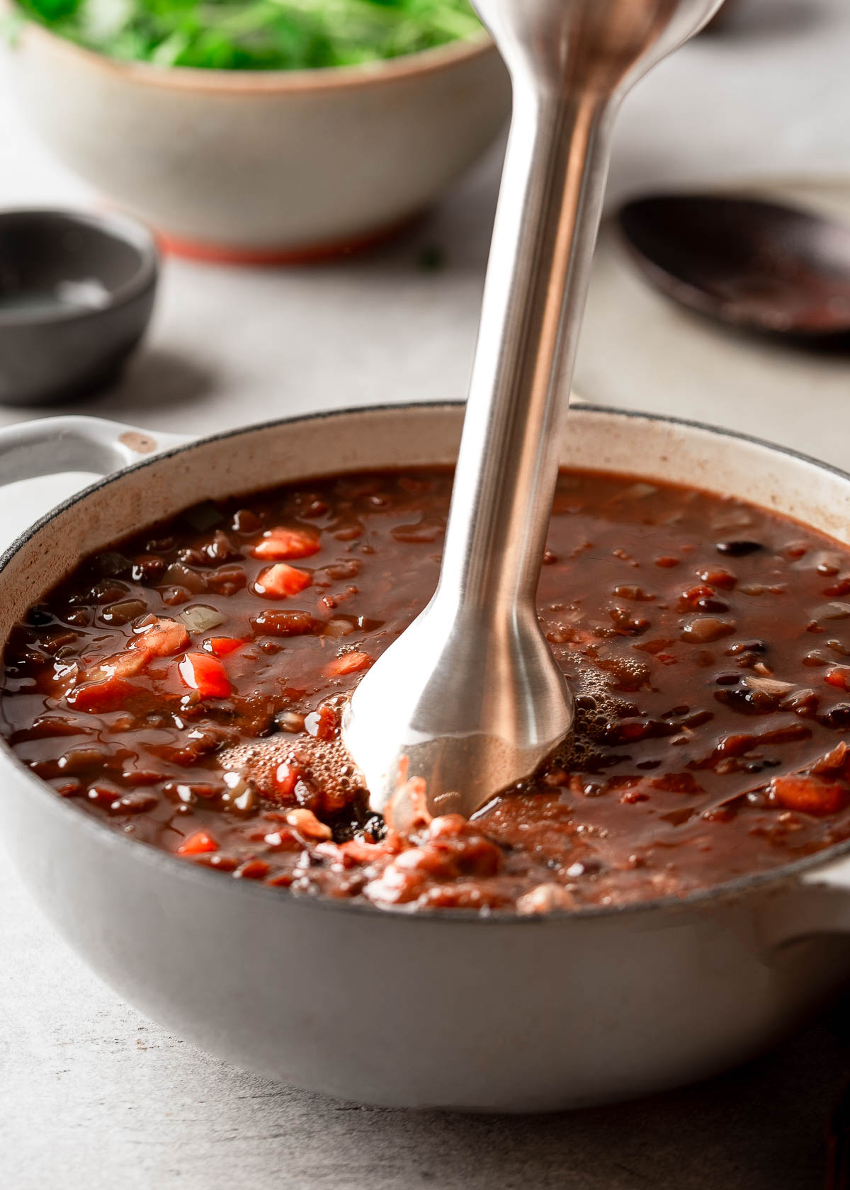 Cooked spicy black bean soup being blended with an immersion blender.