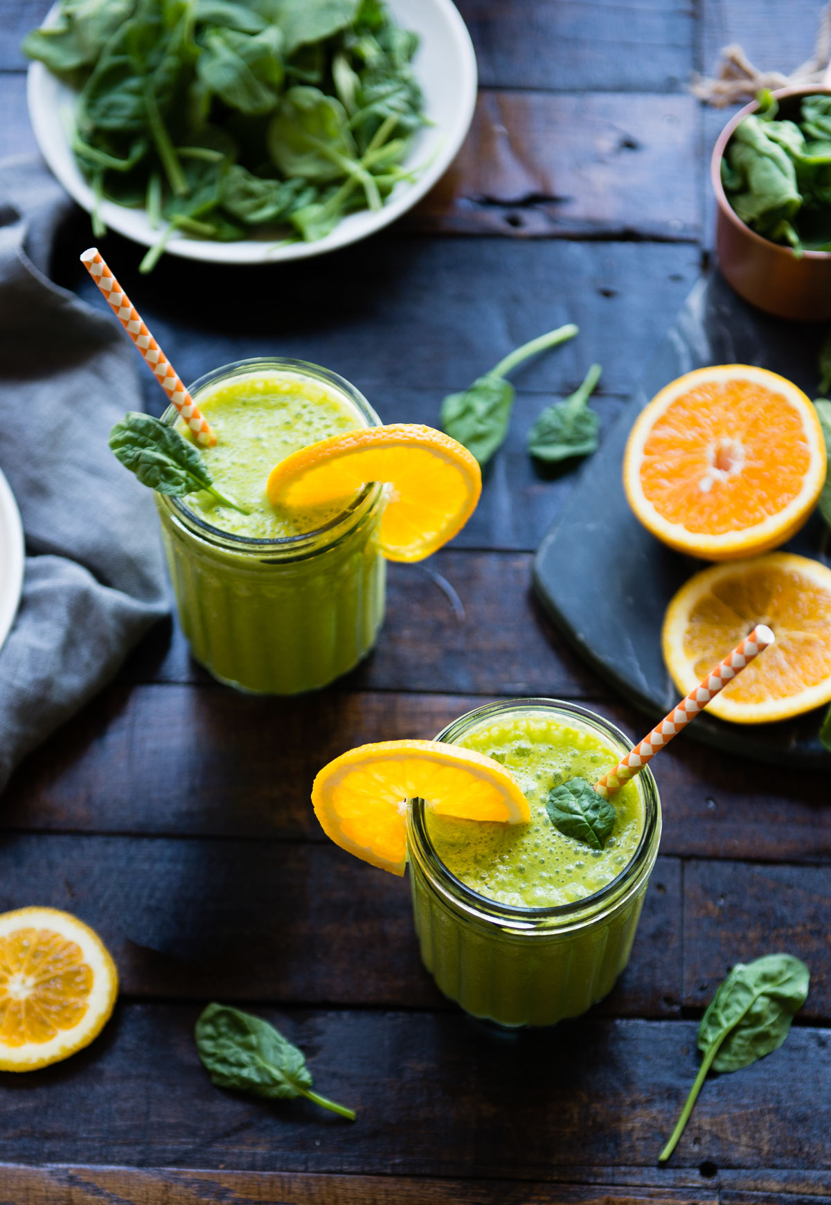 Two Mason jars filled with spinach banana smoothie garnished with orange slice.