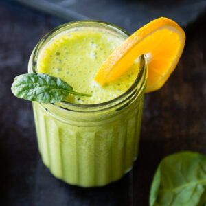 A fun textured Mason jar filled with spinach banana smoothie garnished with an orange slice and a paper straw.
