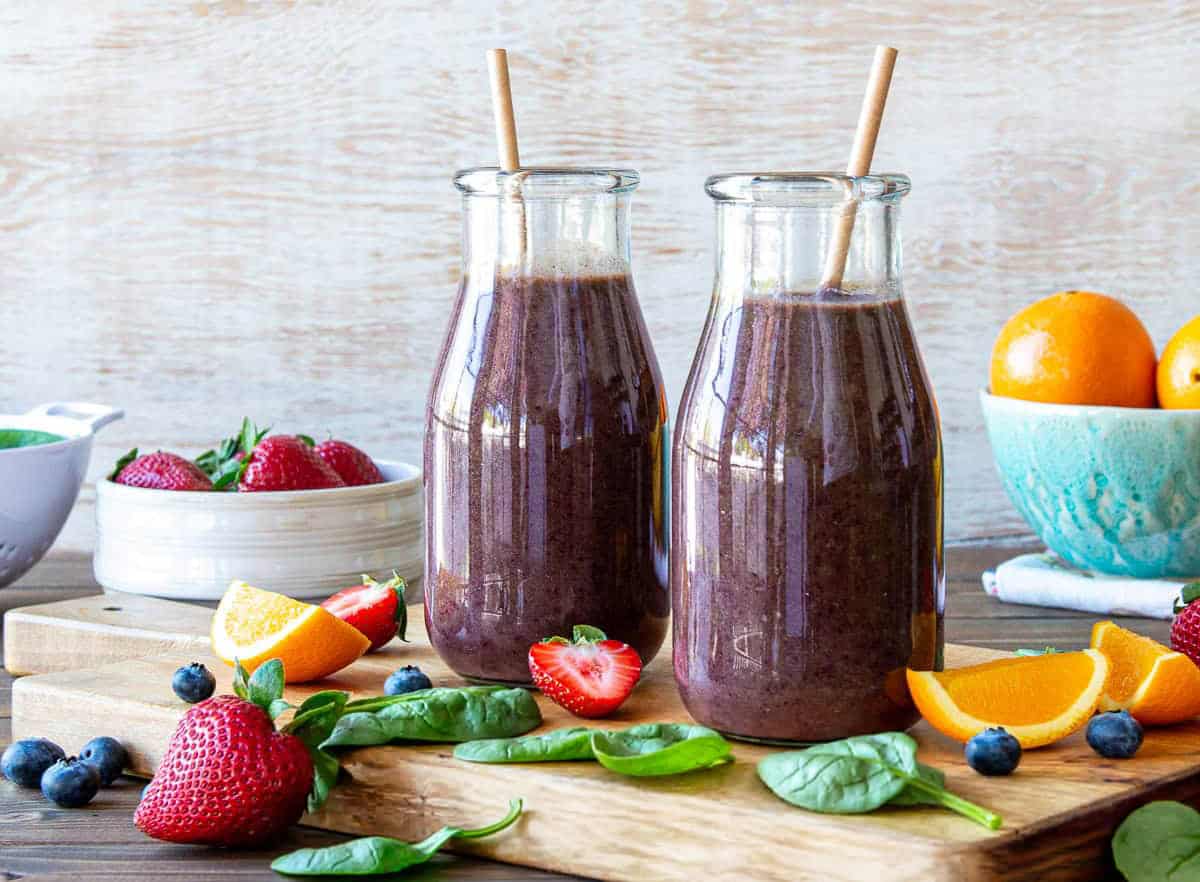 Healthy spinach berry smoothies in glass bottles with fresh fruit around.