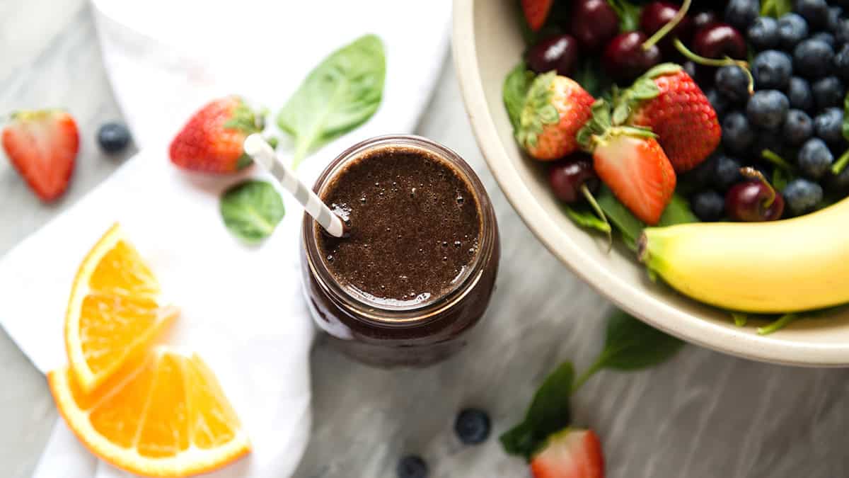 Fresh berries, orange slices, and a green smoothie in a jar on a white surface.
