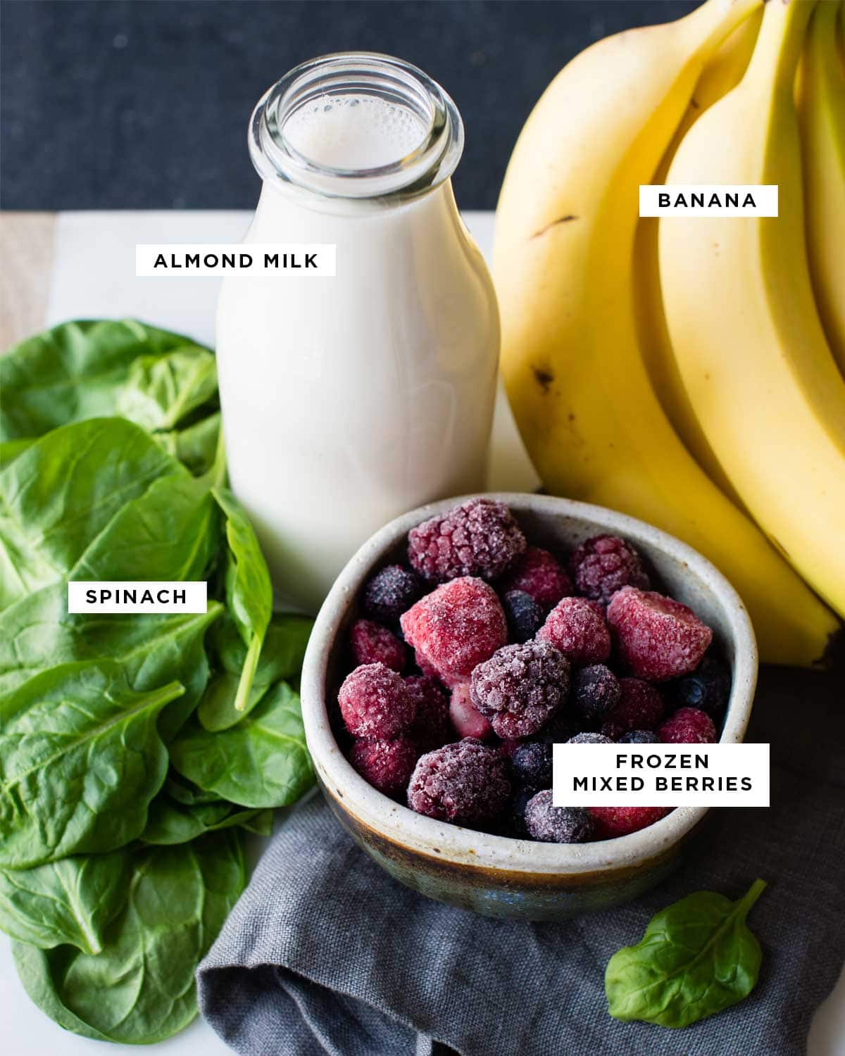 ingredients for a spinach smoothie including spinach, almond milk, banana, and frozen mixed berries.