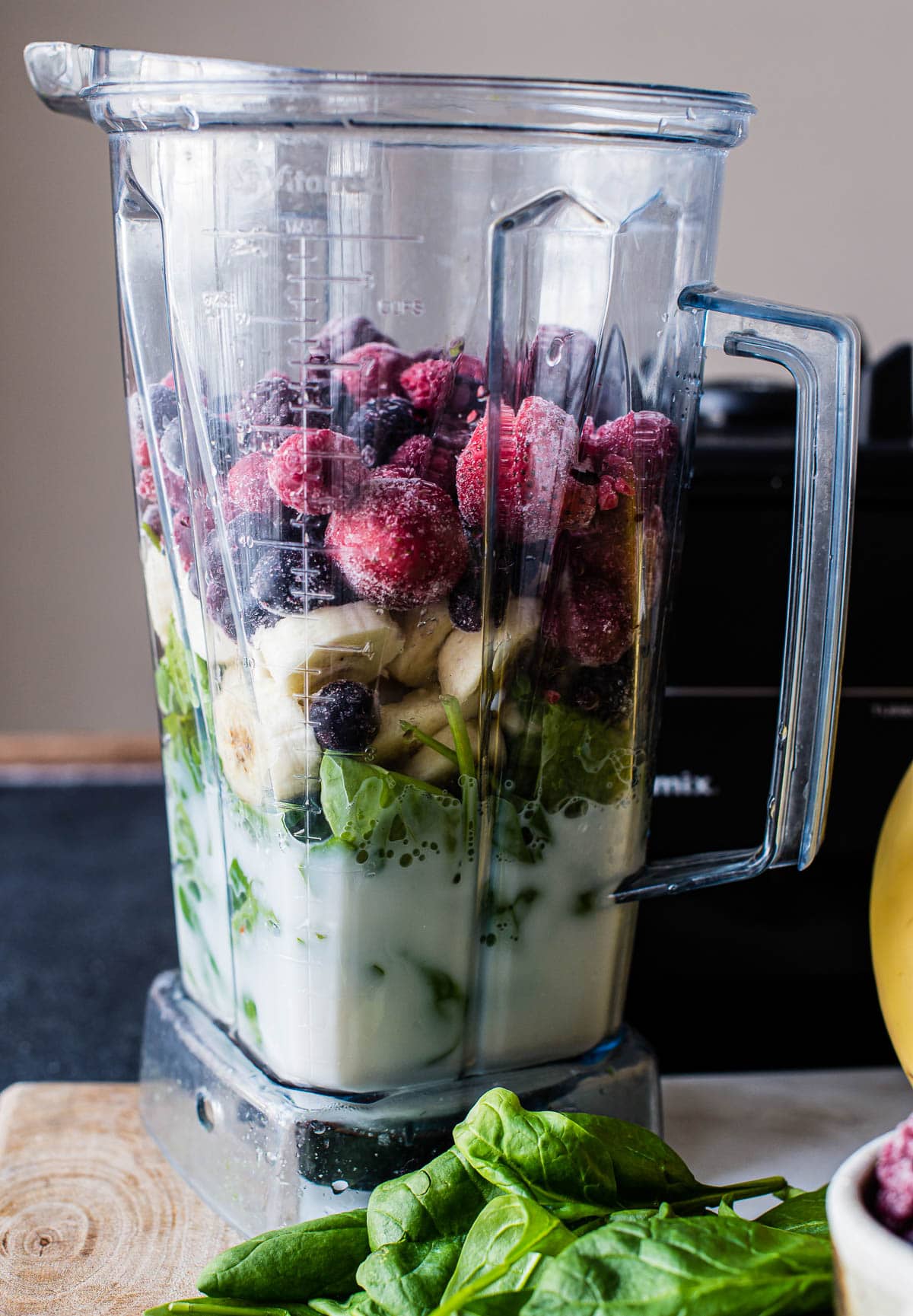 A tall blender on a countertop, filled with smoothie ingredients and ready to be blended for a healthy fruit and spinach smoothie.