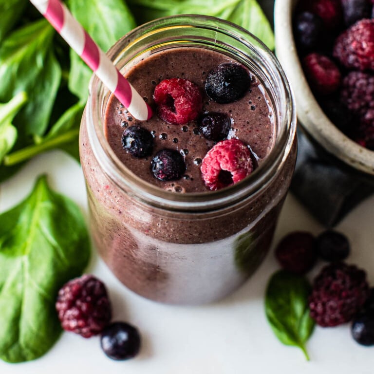 overhead photo of a spinach berry smoothie topped with berries and surrounded by fresh spinach