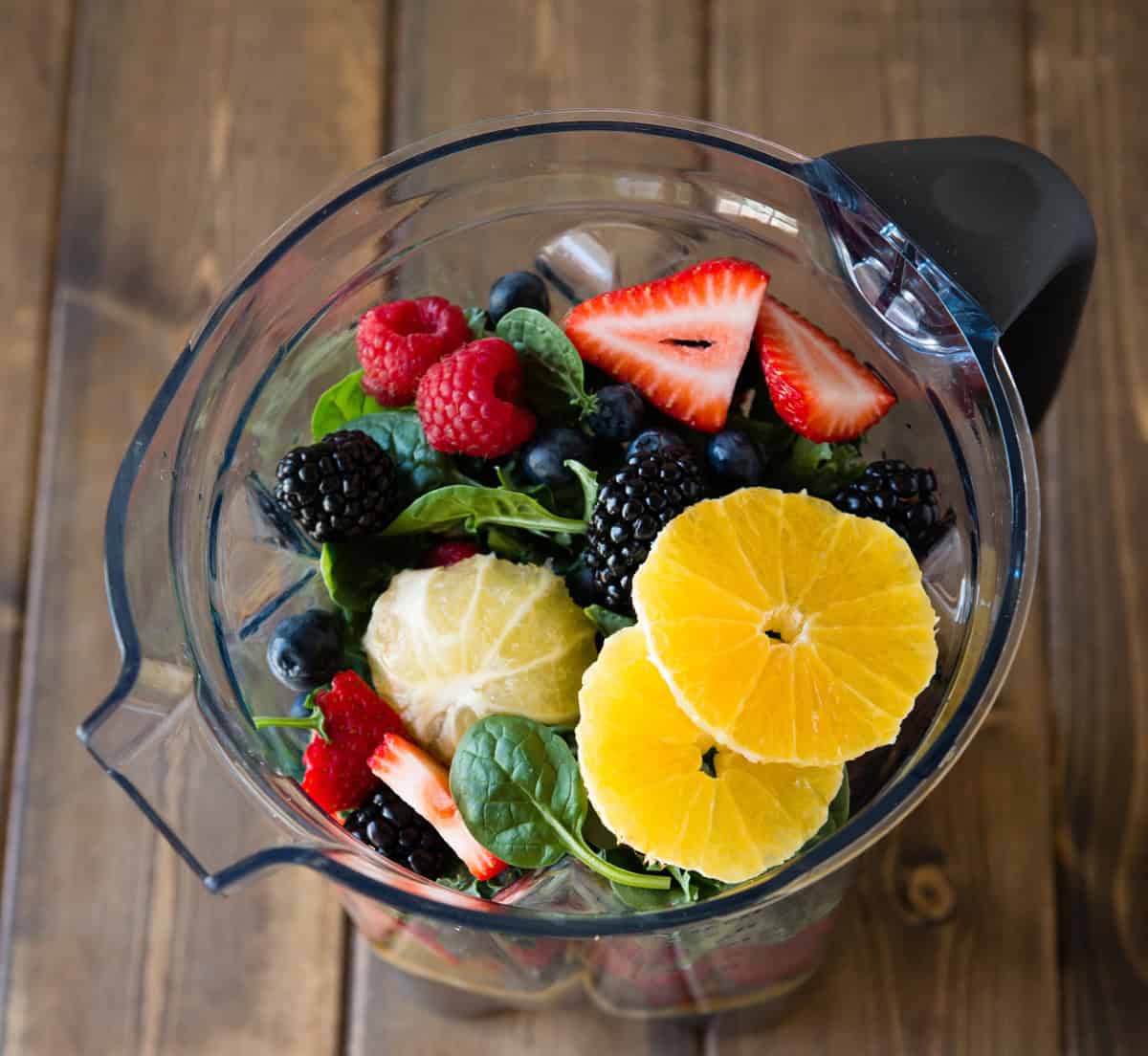 Fresh mixed berries and citrus slices in a blender for a smoothie.