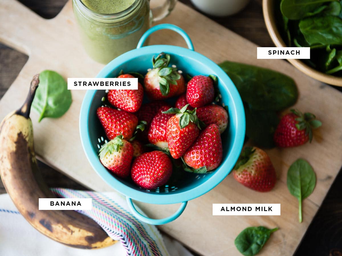 ingredients for a spinach banana strawberry smoothie including spinach, strawberries, banana and almond milk.