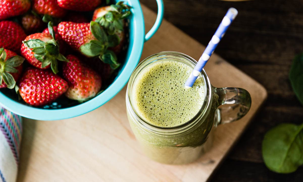 green smoothie with fun paper straw and fresh strawberries next to it.
