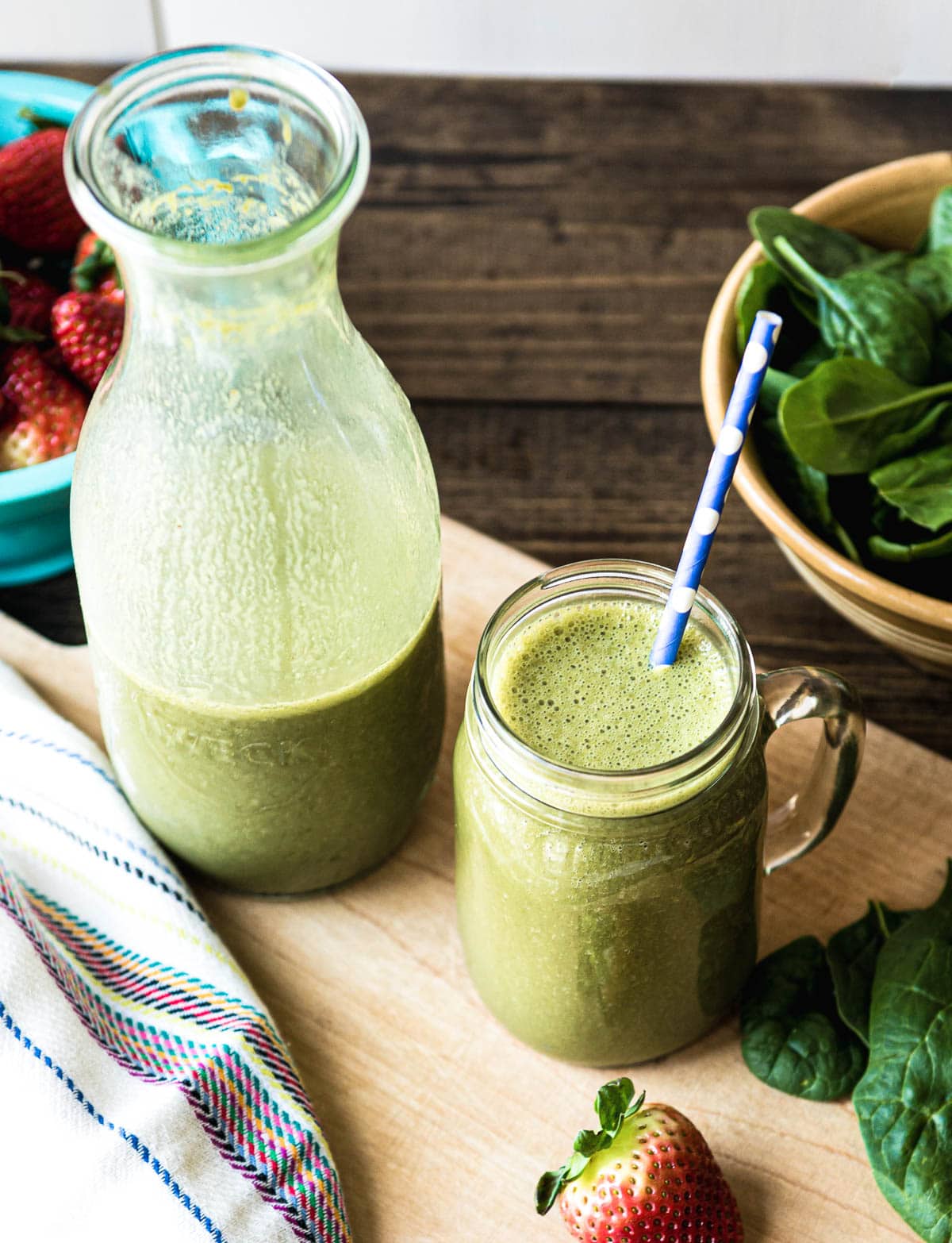 delicious green smoothie for snack or a meal in a glass mug with a paper straw next to a pitcher of green smoothie.