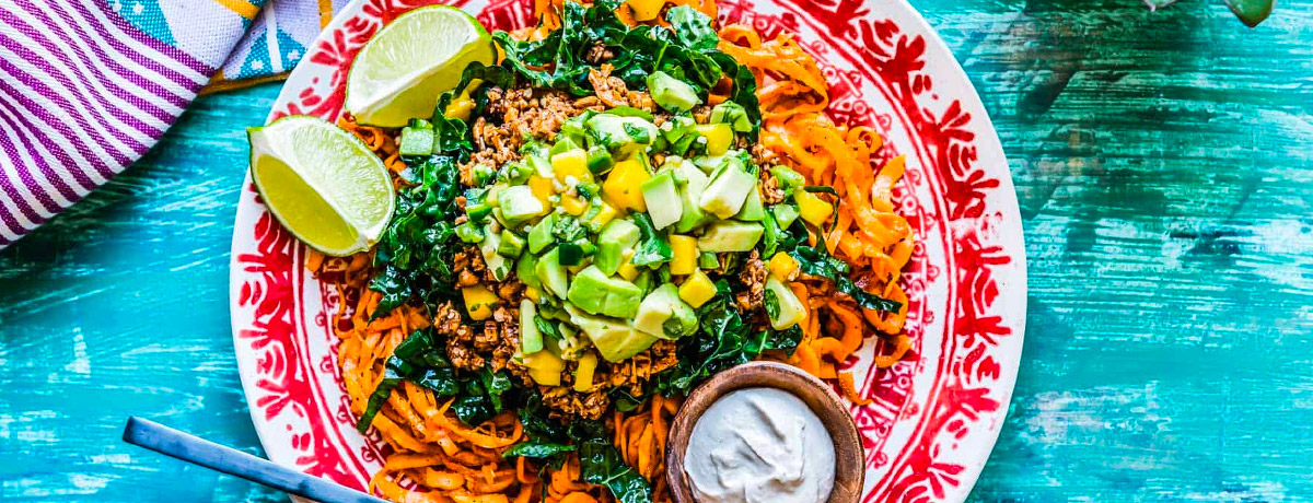 vegan taco salad on a bed of spiralized sweet potatoes with a bright blue background and a bright red plate