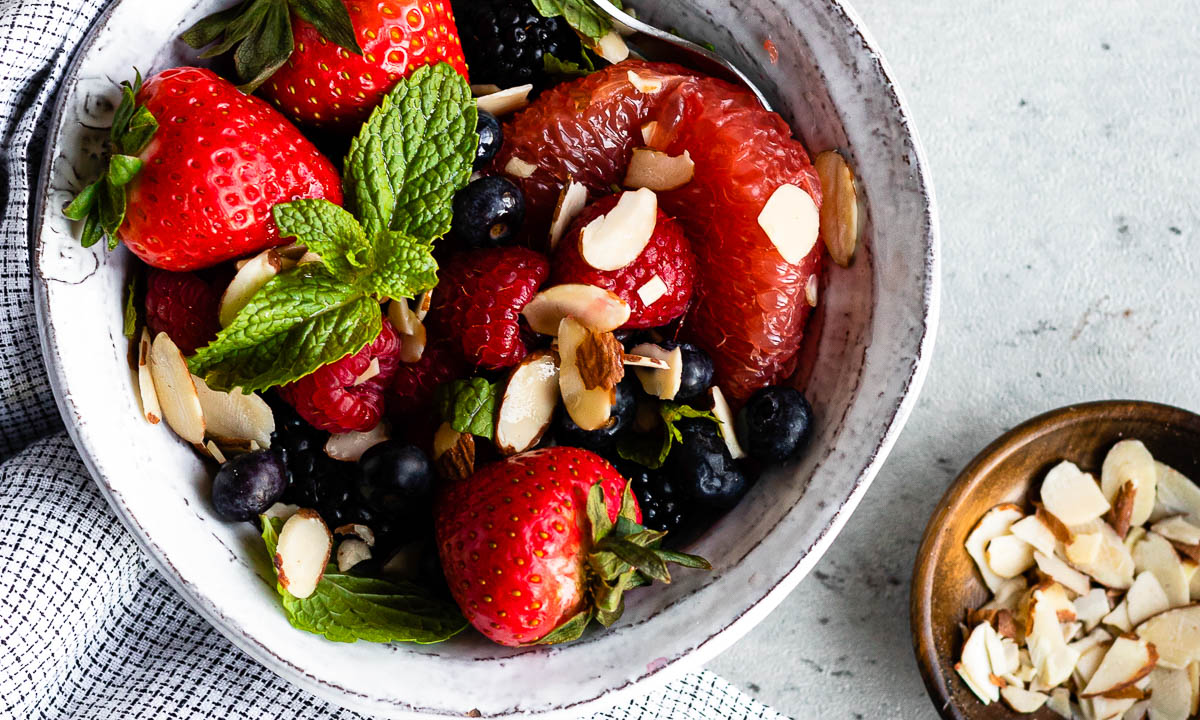 bowl of spring berry fruit salad topped with fresh mint and sliced almonds.