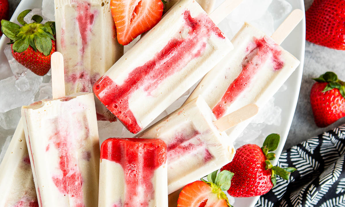 strawberry cream popsicles on a plate of ice surrounded by fresh strawberries.