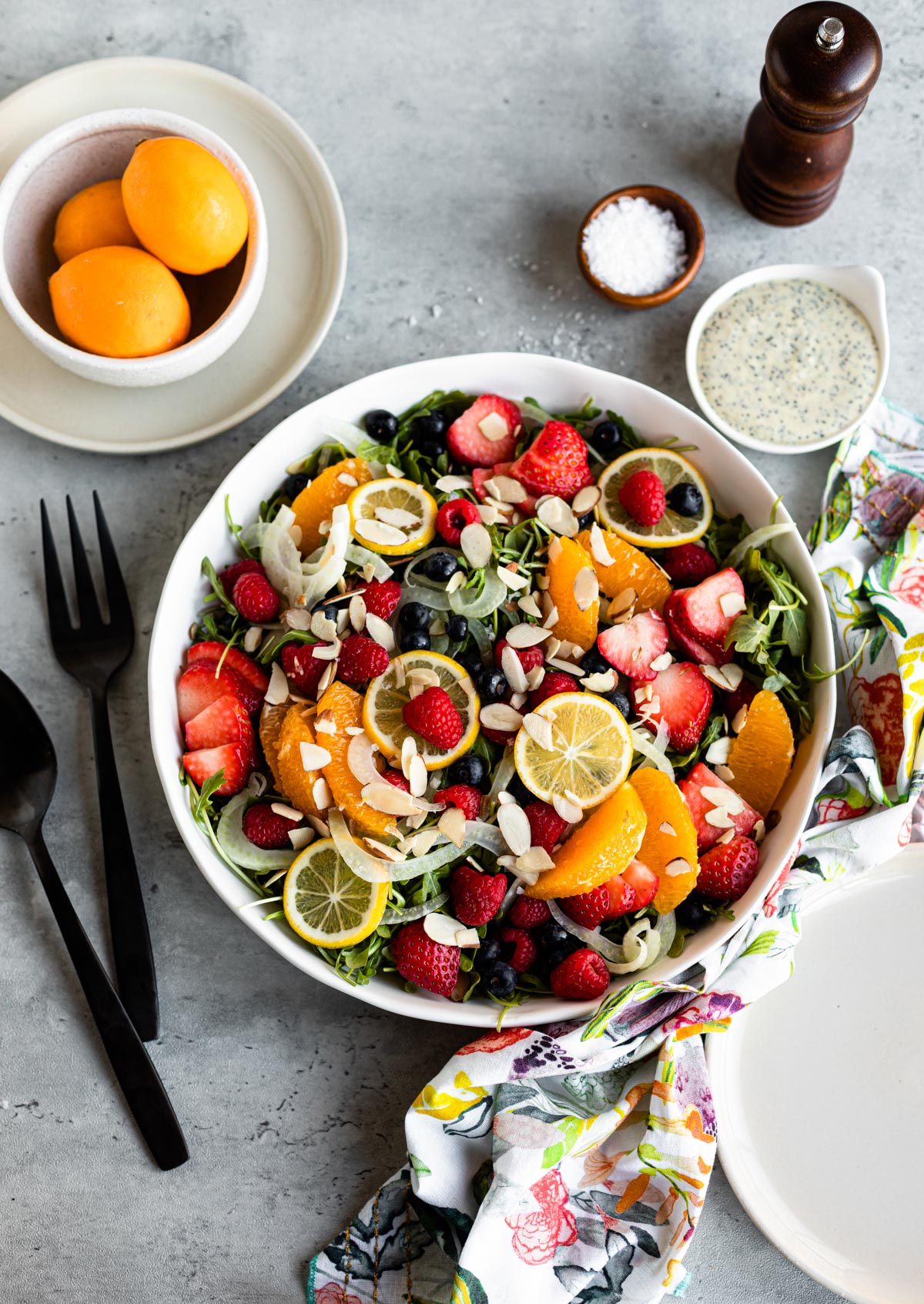 strawberry arugula salad in a large white bowl next to a white cup of salad dressing.