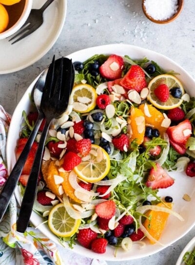 strawberry arugula salad with lemon dressing on a white plate with black utensils.