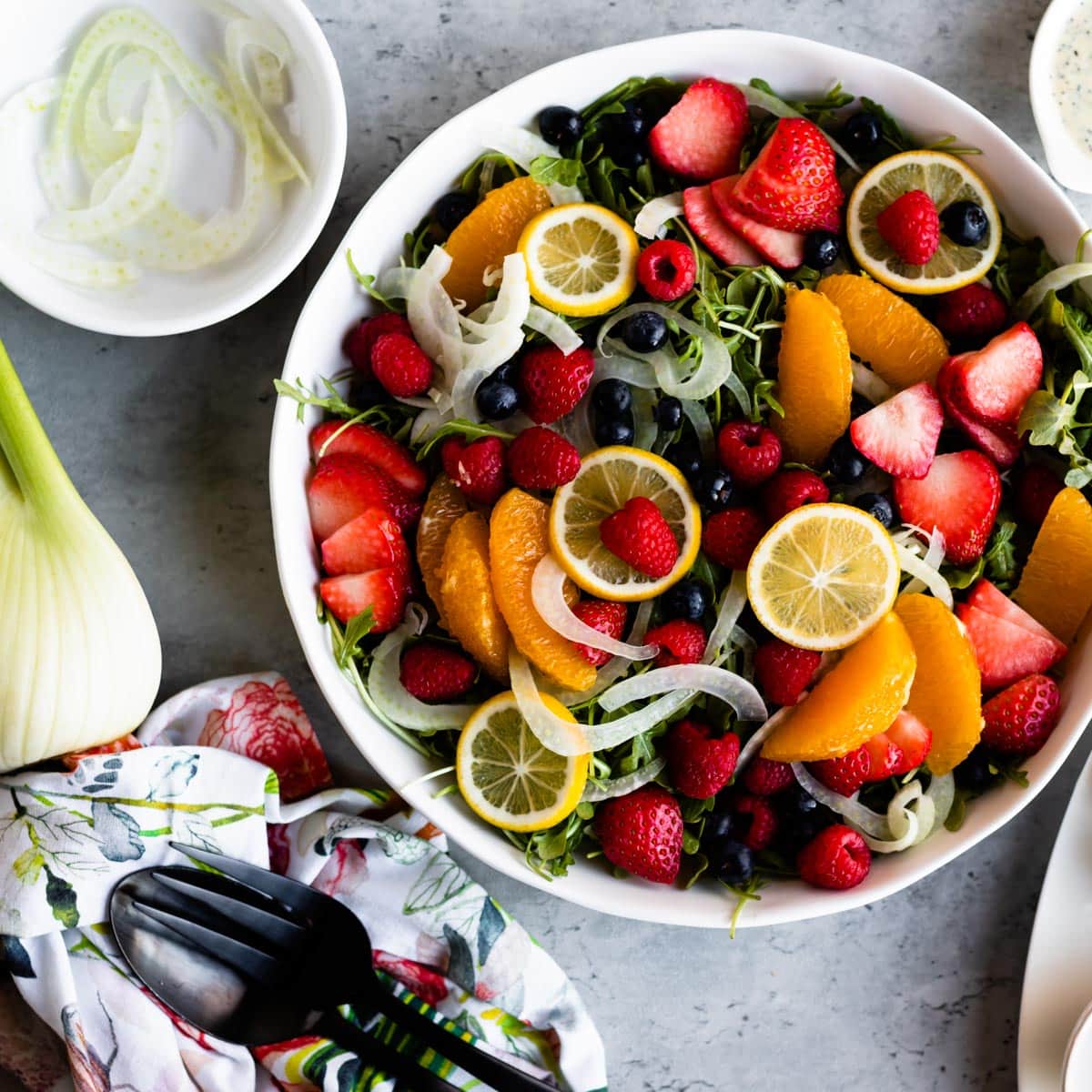 Strawberry arugula salad with fresh cut citrus on concrete counter.