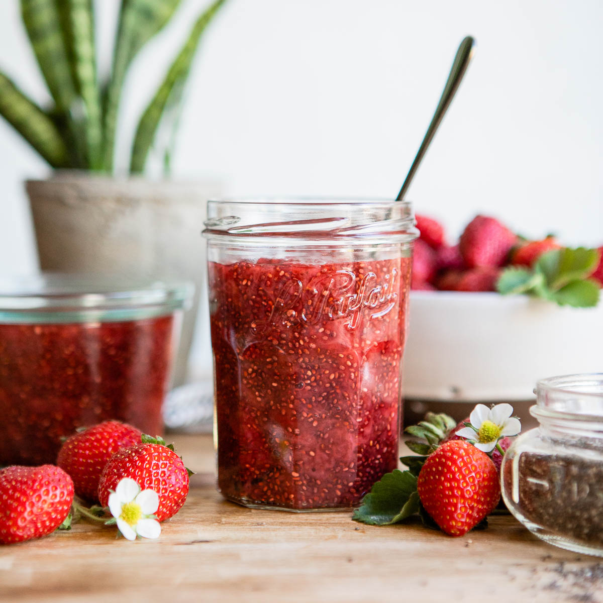 strawberry chia jam in jelly jar with spoon on counter.