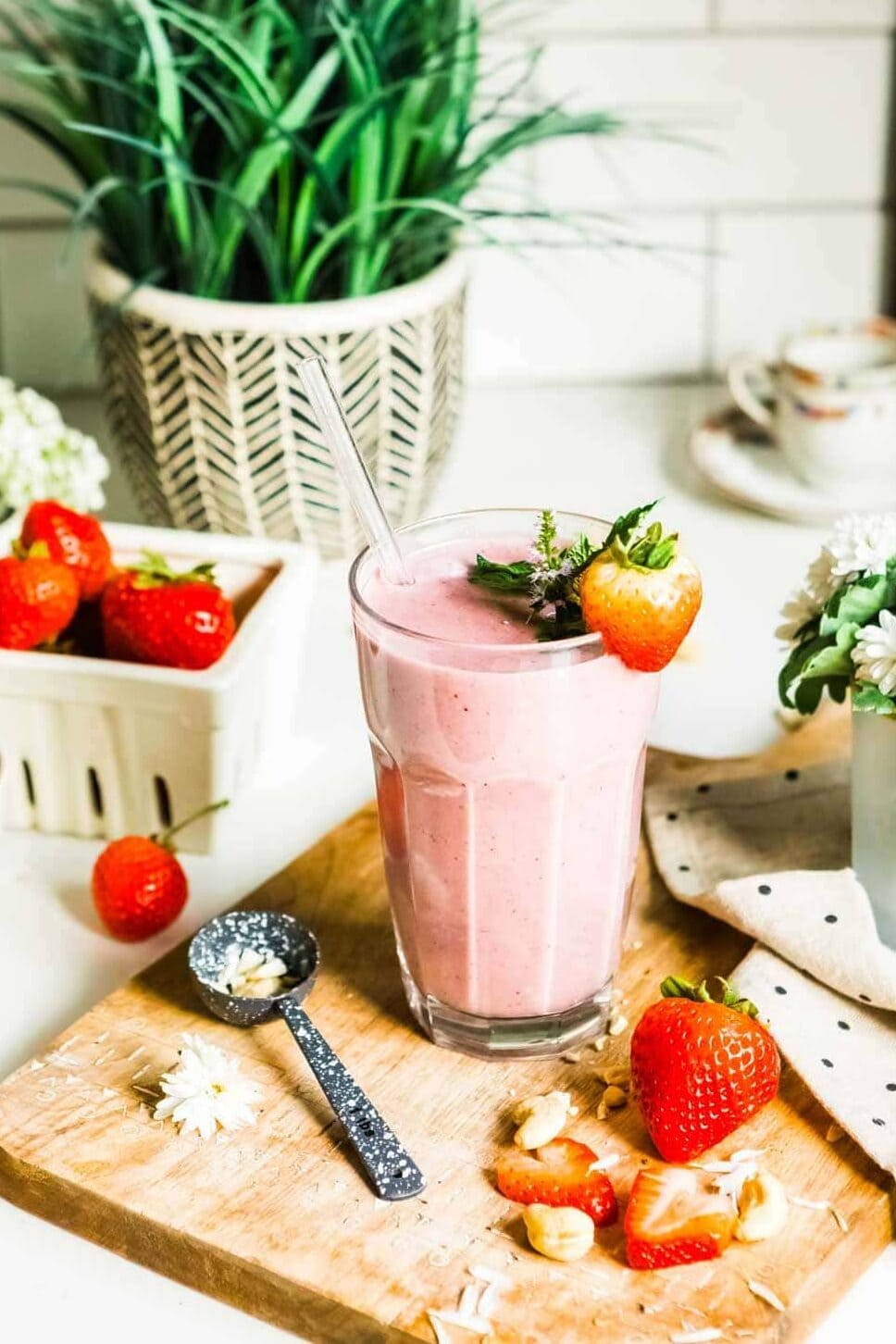 strawberry smoothie in a glass with a glass straw and a strawberry garnish.